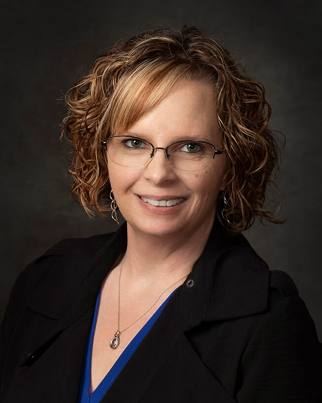 Woman with glasses and short curly hiring smiling into the camera