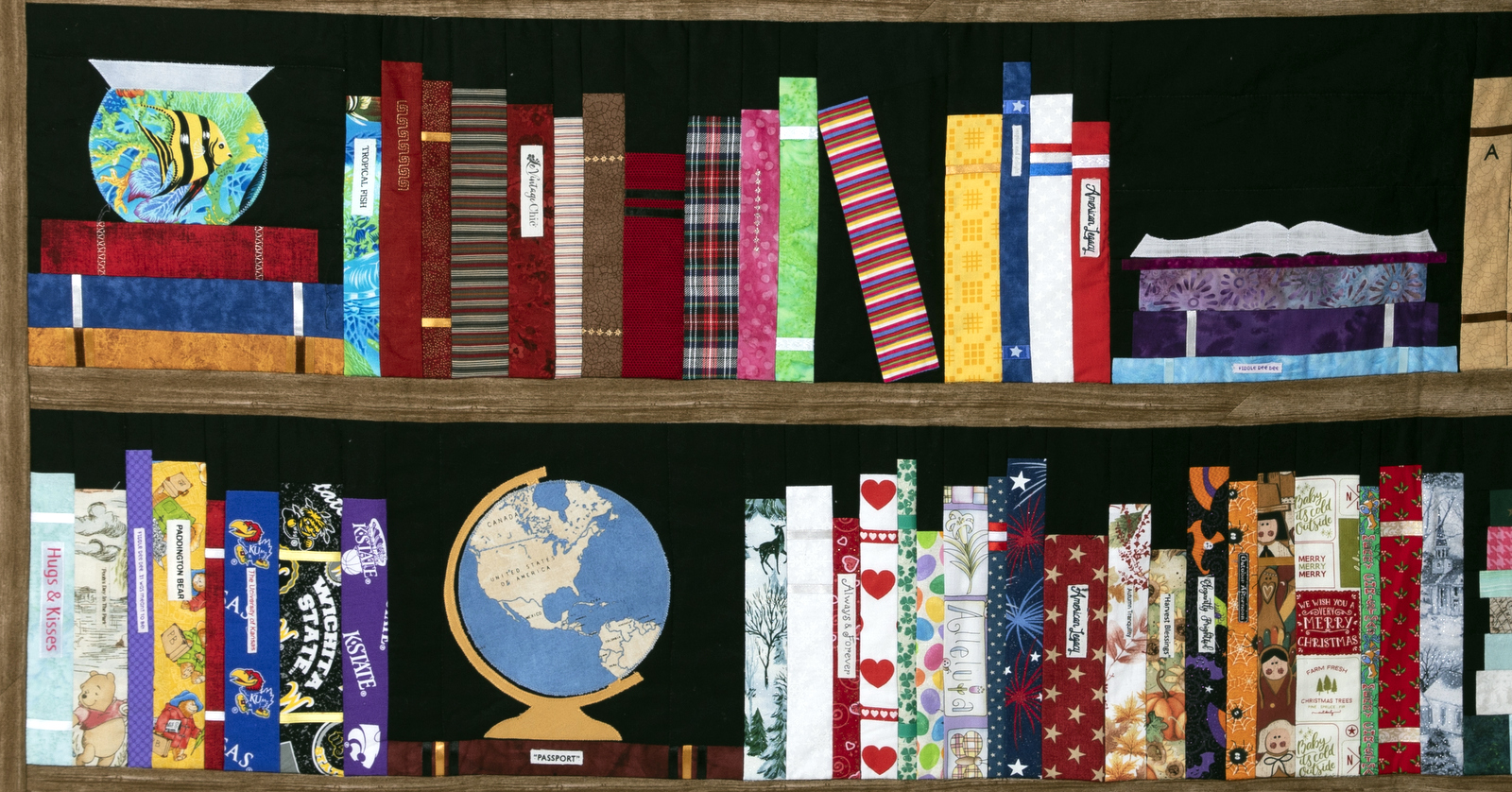 A Bookshelf quilt depicting two shelves of books, a fishbowl, a globe, and various other items. The designs are vibrant, with a mix of patterns and colors for each simulated book cover, adding charming personal details to the colorful display.