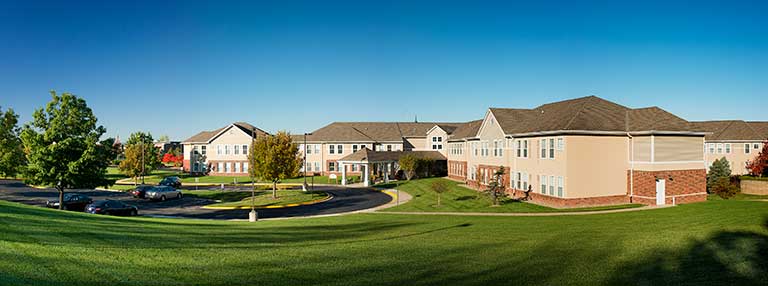 A panoramic view of a residential complex with multiple two-story buildings surrounded by green lawns and trees under a clear blue sky.