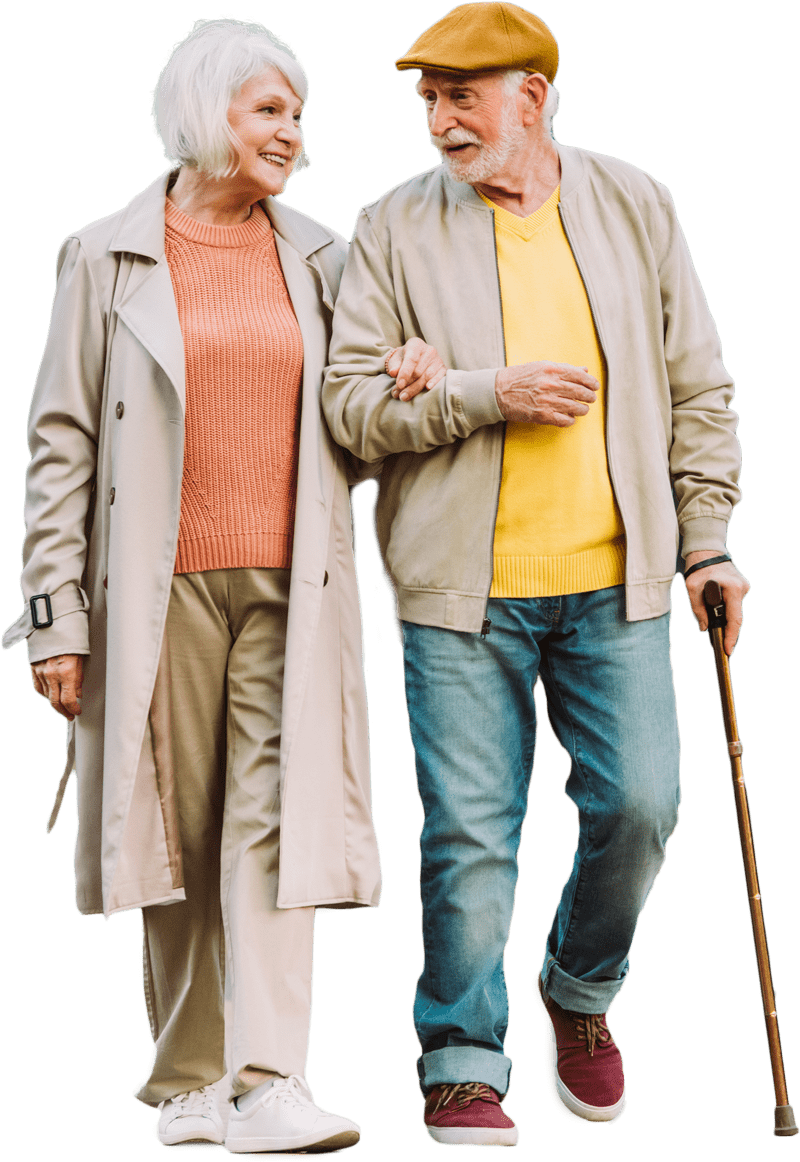 An elderly couple, dressed in casual attire, walks arm in arm. The man uses a cane and wears a yellow sweater and cap, while the woman smiles, wearing a coral sweater and beige coat. They embody the charm of senior living in Colorado.