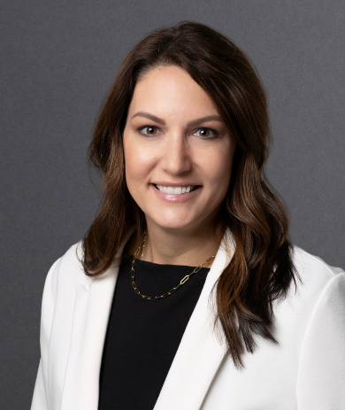 Woman with long dark hair smiles at the camera - she wears white jacket over black top