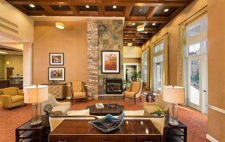 A spacious living area with modern decor, featuring a stone fireplace, seating arrangement, wall art, and large windows allowing natural light.