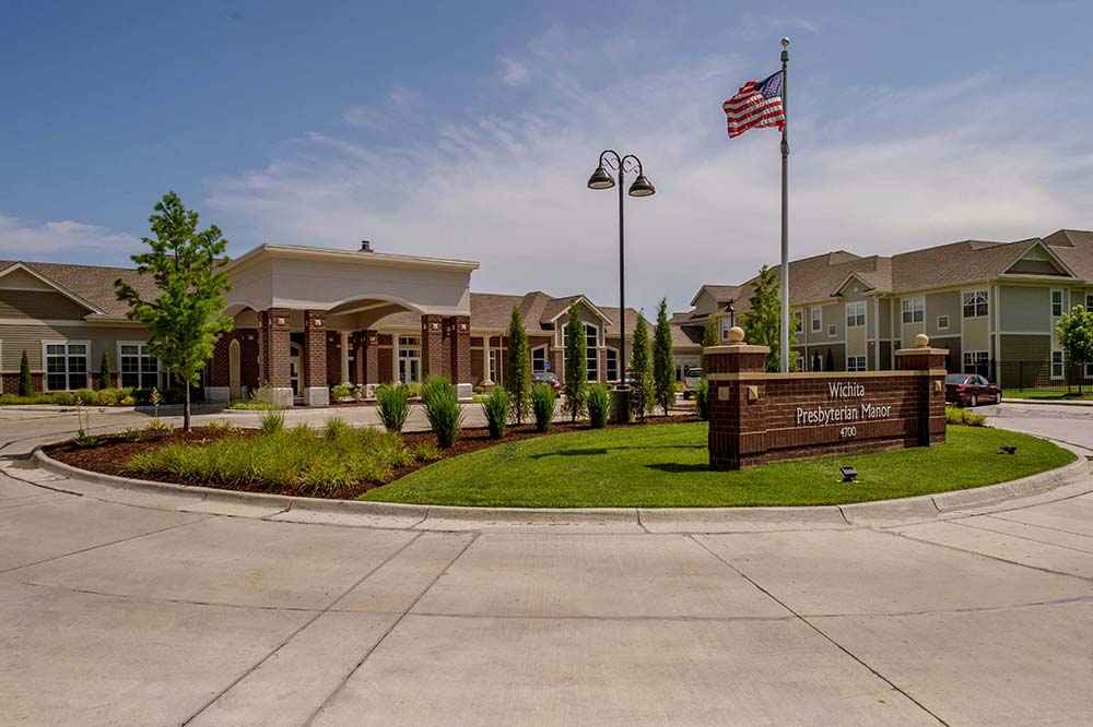 Entrance to Wichita Presbyterian Manor with a flagpole, circular driveway, and building surrounded by light landscaping.