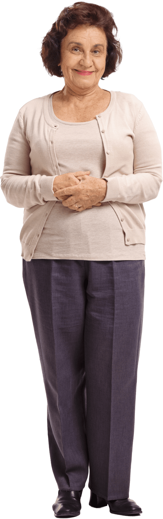 A woman with short, dark hair wearing a light-colored cardigan, a blouse, and dark pants, standing with her hands clasped in front. She exudes the warmth and friendliness of someone who knows the charm of senior living in Kansas.